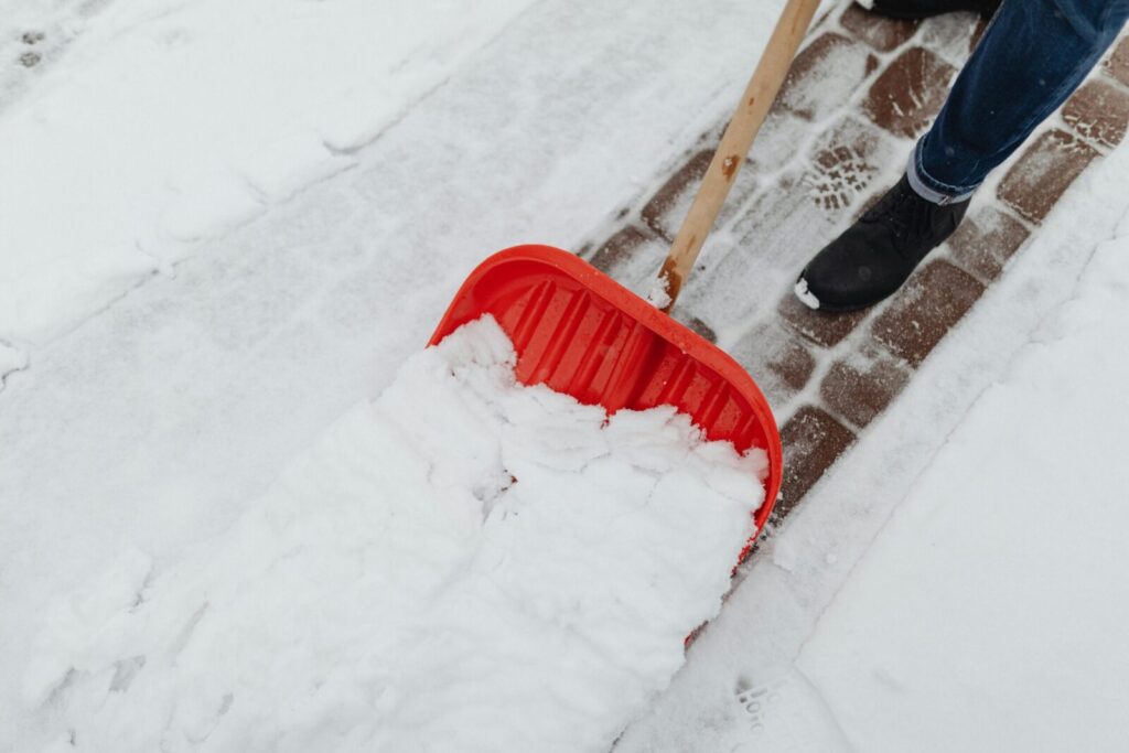 Person using a red snow shovel to clear snow from a driveway in winter.